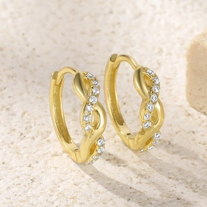 Macro detail of gold twist earrings with small white zircon diamonds on stone surface