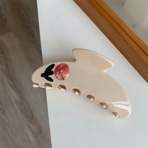 Close-up of cream tulip claw clip with swallow patterns and rhinestone floral detail