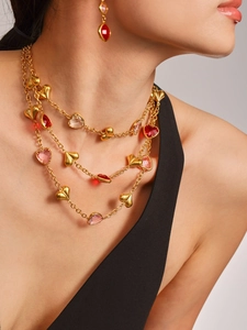 Detalle de collar dorado multicapa con corazones rojos y rosas en una modelo elegante