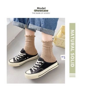 Detail of light brown cable knit crew socks with ruffled cuffs worn with denim and shoes