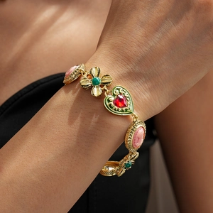 Close-up of vintage gold bracelet featuring red heart gems and pink cameo charm on wrist