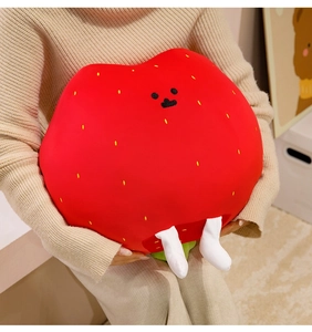 Detail of strawberry plush pillow with cute facial features held by a person at home
