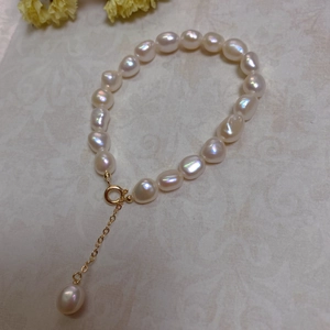 Detail of baroque pearl bracelet with gold clasp and extension chain on neutral surface