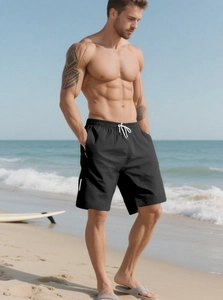 Men's black quick-dry beach shorts with white drawstring shown on a sunny coastal beach