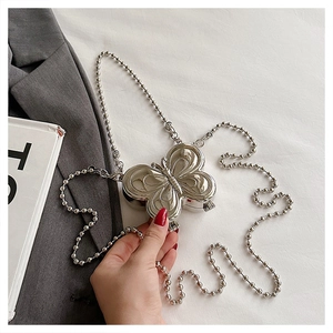 Detail of silver butterfly-shaped metal mini bag with bead chain on grey blazer