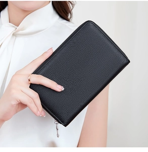 Close-up of black litchi grain leather passport wallet held by a model in white