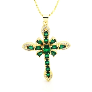 Macro detail of gold cross pendant featuring green pear-cut stones and white zircon accents