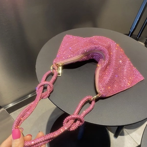 Detail of pink rhinestone handbag with knotted strap and gold zipper on a black table