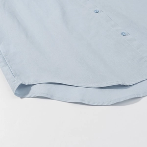 Close-up of light blue shirt buttons and stitched hem showing cotton-linen texture