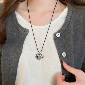 Close-up of heart-shaped leopard print pendant necklace on a black wax cord worn by model