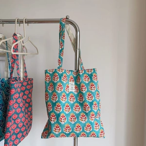 Detail of teal cotton tote bag with floral block print and white woven label logo