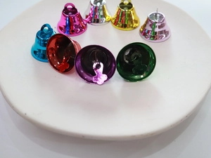 Macro shot of 26mm matte colorful metal christmas bells with hanging loops on ceramic plate