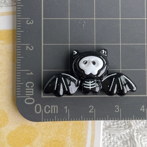 Macro shot showing 4cm black skull bat resin charm on a metric scale cutting mat
