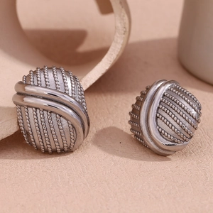 Dettaglio di orecchini ovali a bottone color argento con trama intrecciata e linee