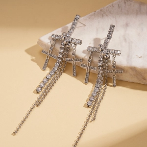 Close-up of silver tassel earrings with rhinestone cross charms on marble stone
