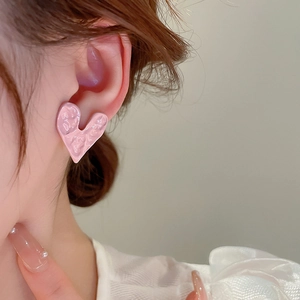 Close-up of pink heart stud earrings with hammered texture worn by a model