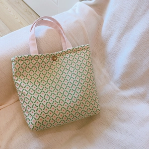 Floral canvas lunch bag with green leaf pattern and pink handles on a soft knit background