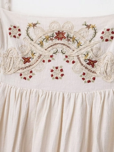 Close-up of floral embroidery and pleated details on a beige cotton linen dress