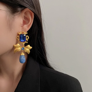 Close-up of vintage gold earrings with blue square gems and drop pendants on model