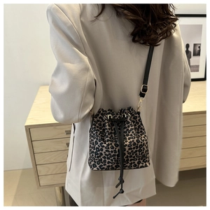 Détail du sac seau léopard avec fermeture à cordon porté sur un blazer beige