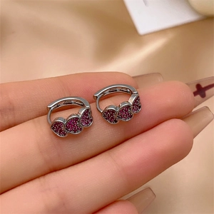 Macro shot of silver triple heart earrings with red zircon held by hand on satin