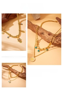 Detail of layered gold-plated necklaces with Hamsa hand and evil eye charms on wood