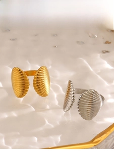 Détail de bagues coquillages dorées et argentées sur un plateau en verre ondulé