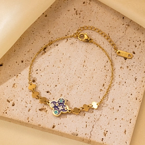 Detalle de pulsera de acero inoxidable dorado con dije de flor morada y pequeñas flores de oro
