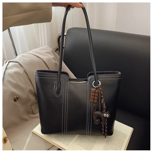 Close-up of black leather tote bag with white contrast stitching and charm details