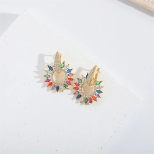 Dettaglio di orecchini dorati con pietre di zircone multicolore su fondo pietra