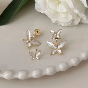 Detailed close-up of white enamel butterfly earrings with gold plating on a ceramic tray