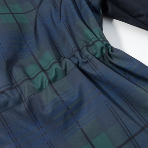 Close-up of the dark blue plaid fabric detail and waist stitching on the windbreaker coat