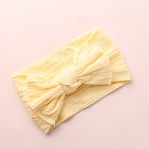 Detail of light yellow knitted baby headband featuring a large bow on pink background