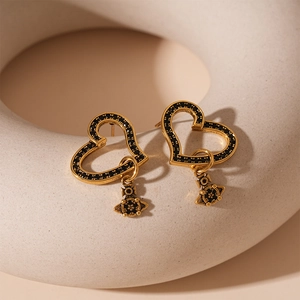 Detail view of heart-shaped gold earrings with black crystals and Saturn pendant