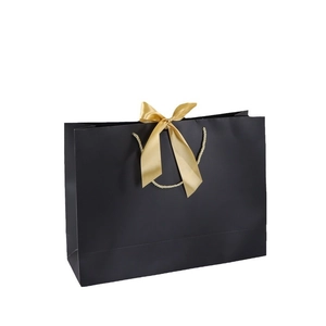 Elegant black paper gift bag with golden ribbon bow accent on a clean white background