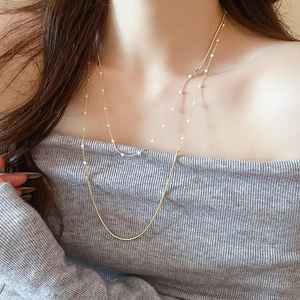 Close-up of double-layered gold snake chain necklace with elegant white pearls on a model