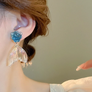 Detail of blue acrylic rose and iridescent fishtail earrings worn by a model
