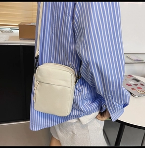 Detail of adjustable nylon strap and front zip pocket on a cream crossbody bag