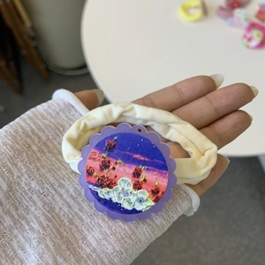 Detail of a white elastic scrunchie featuring a purple wavy charm with red mushroom art