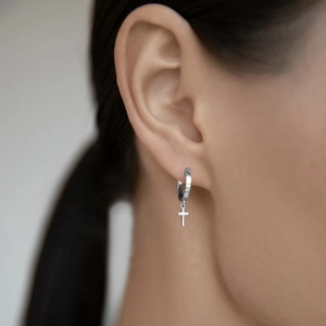 Close-up of sterling silver cross hoop earrings worn by a model with soft lighting