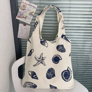 Detail of canvas tote bag with blue seashell prints hanging on a white chair
