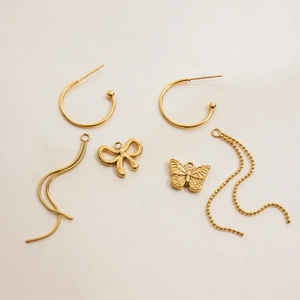 Detail of 18K gold stainless steel hoop earrings with bow and tassel charms on beige paper