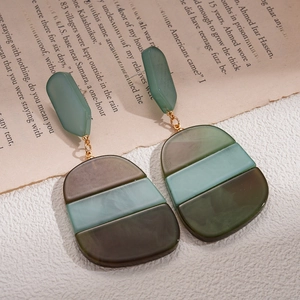 Close-up of geometric acetate earrings with green amber texture on vintage paper
