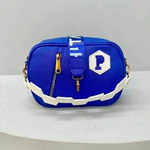 Detail of royal blue nylon crossbody bag featuring white zigzag handle and golden hardware