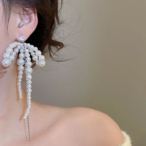 Close-up of elegant bow pearl tassel earrings in silver finish on model's ear