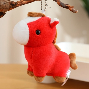 Close-up of red plush pony keychain with white markings and soft texture on wooden branch