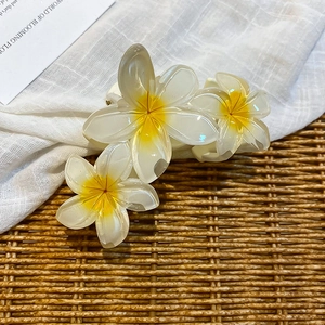 Detail of tropical frangipani hair claw clip with white resin petals and yellow center