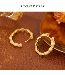 Macro detail of brushed gold earrings with inlaid zircons on a leather surface