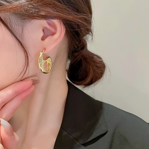 Close-up of golden geometric hollow heart tassel earrings worn by a model