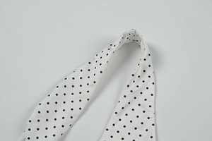 Detailed close-up of white fabric with black polka dots and fine stitching on the strap
